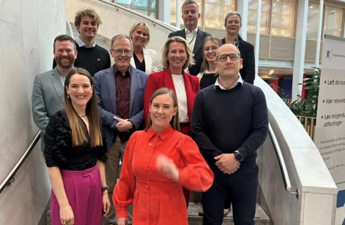 Barne- og familieminister Lene Vågslid med gruppen som utgjør det nasjonale partnerskapet. Prosjektleder Solveig Korum foran til venstre. Foto: KS En rekke mennesker i en trapp smiler mot kameraet.