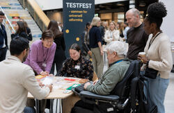 Testfest bringer mennesker sammen i en uformell ramme: testere og tjenesteeiere, brukere og utviklere. I dette møtet oppstår forståelse, tillit og ofte et sterkt engasjement for å forbedre tjenestene. Foto: KI-generert En mangfoldig gruppe mennesker møtes rundt et bord på Testfest for å teste og lære om universell utforming i et inkluderende miljø.