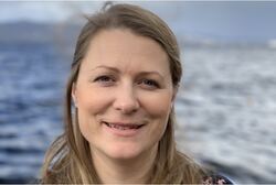 Kvinne med langt blondt hår med sjø i bakgrunnen.