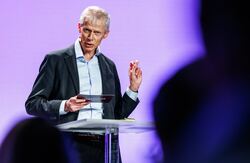 Kunstig intelligens er, ifølge Hans Christian Holte, en av de store samfunnsutfordringene i vår tid. Derfor må Norge løfte de viktige debattene, legge grunnlaget for gode beslutninger og bygge en utvikling som både er rask og ansvarlig. Foto: Kilian Munch, Digitaliseringskonferansen Middelaldrende mann i dress på scenen. Blå bakgrunn