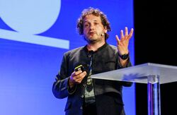 Budskapet fra Michael Riegler var tydelig: Trygg KI-bruk krever ikke bare gode modeller, men gode evalueringssystemer, lokal kompetanse og kontinuerlig testing i den virkeligheten teknologien faktisk skal brukes i. Foto: Kilian Munch, Digitaliseringskonferansen Relativt ung mann med halvlangt hår med krøller på talerstolen.