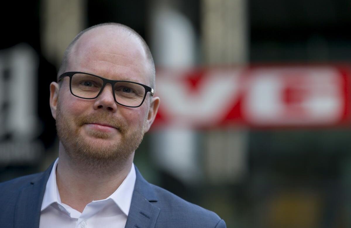 Budskapet til Gard Steiro var klart: I en kunstig virkelighet blir redaktørstyrt journalistikk ikke mindre viktig, men mer avgjørende. Mediene må være et bolverk mot desinformasjon, men de kan ikke gjøre det alene dersom plattformene samtidig styrer offentligheten. Foto: Kilian Munch, Digitaliseringskonferansen Skallet mann med skjegg, dress og hvit skjorte. Uklar VG-logo i bakgrunnen.