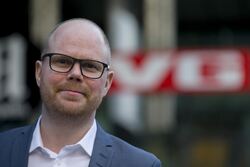 Budskapet til Gard Steiro var klart: I en kunstig virkelighet blir redaktørstyrt journalistikk ikke mindre viktig, men mer avgjørende. Mediene må være et bolverk mot desinformasjon, men de kan ikke gjøre det alene dersom plattformene samtidig styrer offentligheten. Foto: Kilian Munch, Digitaliseringskonferansen Skallet mann med skjegg, dress og hvit skjorte. Uklar VG-logo i bakgrunnen.