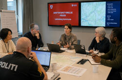 For Lørenskog ble angrepet en brutal påminnelse om hvor avhengig en moderne kommune er av digitale systemer. Men også om hvor avgjørende menneskene er når teknologien svikter. Foto: KI-generert Kriseledelsen i Lørenskog kommune er samlet rundt et bord. Skjermer viser driftsforstyrrelser og kart, mens ansatte og politi diskuterer situasjonen og tar beslutninger under tidspress.