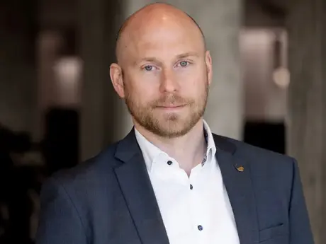 Mann med dress, skallet, blå øyne, ser inn i kameraet.