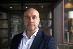 Alvorlig middeladrende mann med dress ser inn i kameraet.