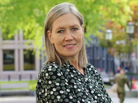 Smilende kvinne med langt lyst hår og blomstrete skjort fotografert utendørs.