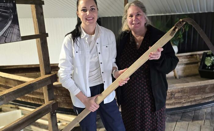 Lilliann Sørensen fra Tanghuset Arena (t.v.) og Margit Langseth fra ungdomslaget Bølgen. De holder en tangljå som ble brukt til tangskjæring og står foran en av få tangprammer som fortsatt eksisterer.