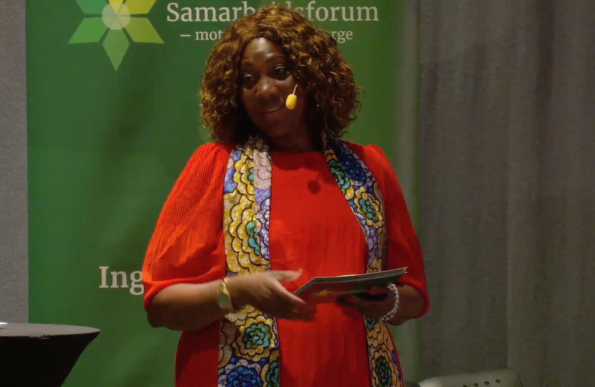 Honoratte BNN Muhanzi var ordstyrer under panelsamtalen. Hun er leder av Bibi Amka og medlem av Samarbeidsforum mot fattigdom i Norge. Foto: Klipp fra video av samtalen. Bildet er av ordstyreren. Hun er farget, muligens afrikansk bakgrunn. Fargerikt kledd.