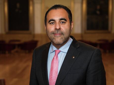 Bildet viser Masud Gharahkhani. Han er opprinnelig fra Iran, og har mørkt hår og brune øyne. Han er ubarbert. Bildet er tatt på Stortinget, vi kan se deler av dressjakka, som er mørk, og den blå skjorten og det rosa slilpset.