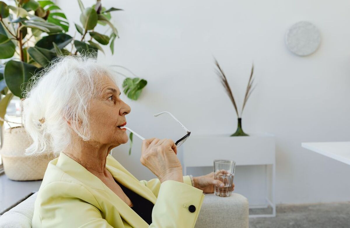 Mange fortsetter å jobbe når de opplever at kompetansen deres trengs. Vis konkret at seniorenes erfaring, relasjoner og kunnskap har verdi for virksomheten. Foto: KAROLINA GRABOWSKA KABOOMPICS / Pexels Eldre kvinne i en stilfull innendørs setting, iført briller og en lys grønn blazer.