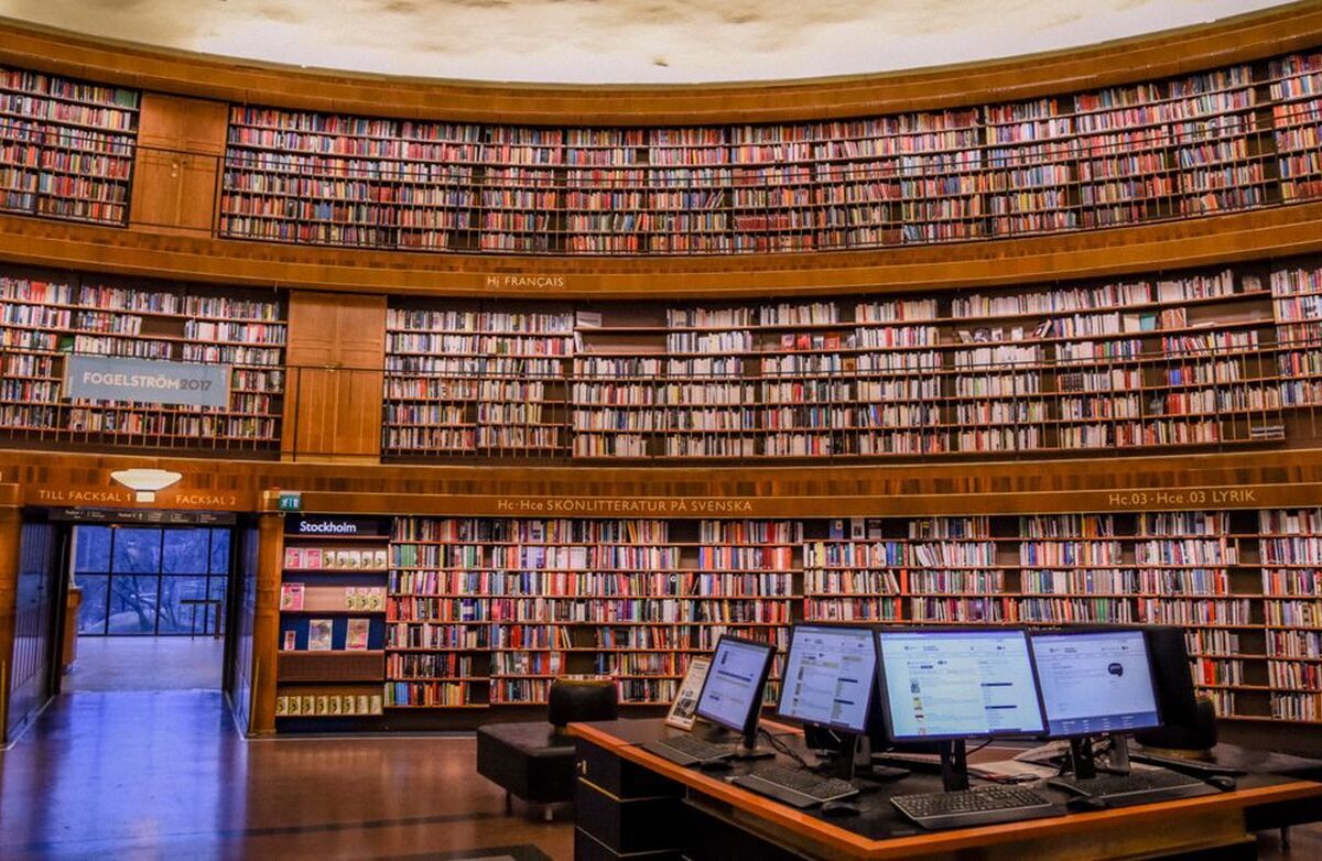 Fra et bibliotek med masse bøker i en halvsirkel fra gulv til tak. Noen PC-er i forgrunnen.