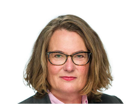 Portrett av Tine Sundtoft med briller og skulderlangt hår, fotografert mot lys bakgrunn. Hun har mørk jakke og en lys rosa skjorte.