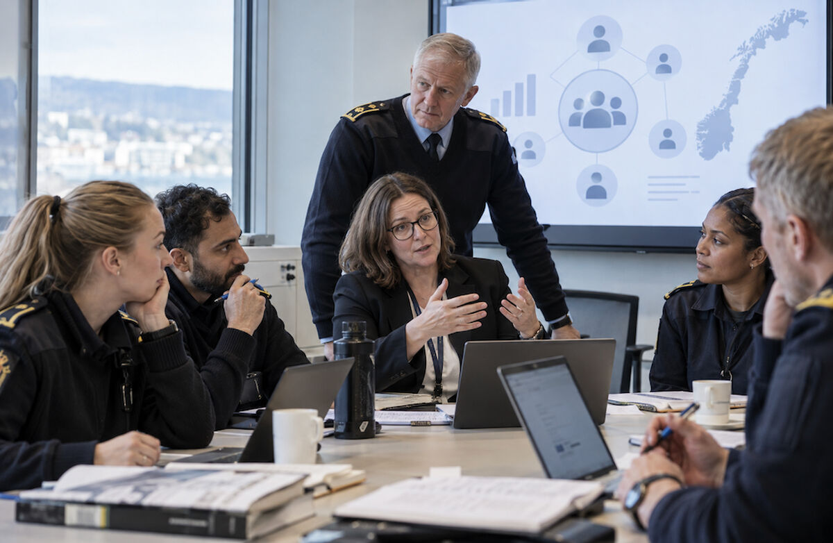 Reform handler ikke bare om nye strukturer og formelle vedtak. Kultur, kompetanse, ledelse og etablerte praksiser påvirker hva som faktisk skjer når reformideene møter organisasjonens hverdag. Foto: KI-generert Et team av politifolk og en sivil leder sitter i møte rundt et bord med PC-er og papirer, mens en skjerm i bakgrunnen viser organisasjonsgrafikk og et kart over Norge.