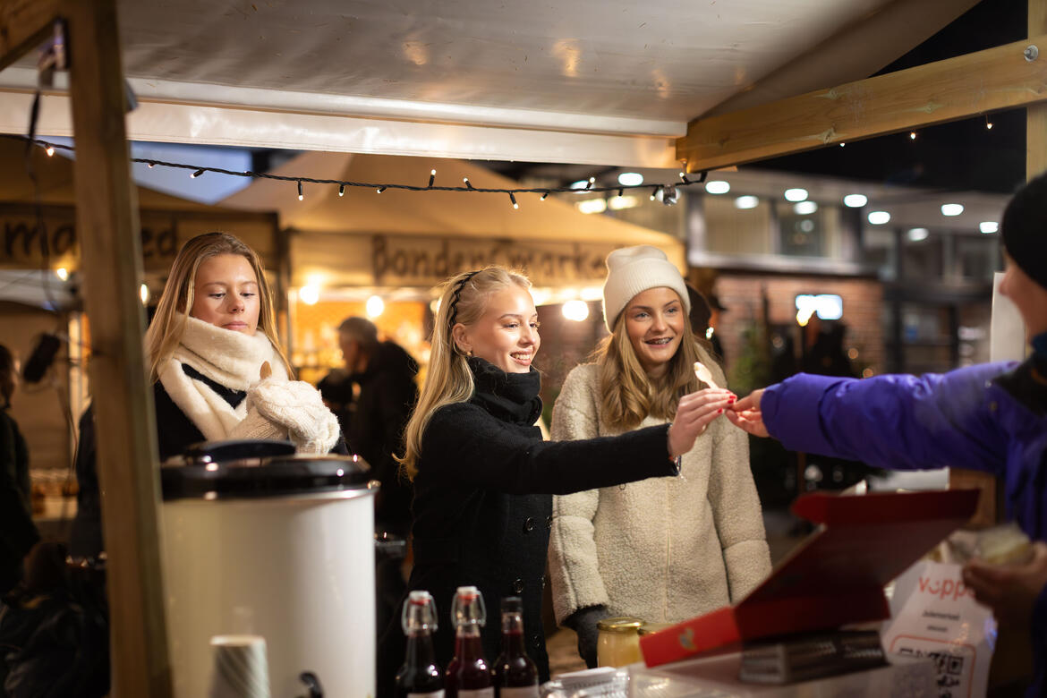 Foto av tre jenter som får smaksprøver fra en bod