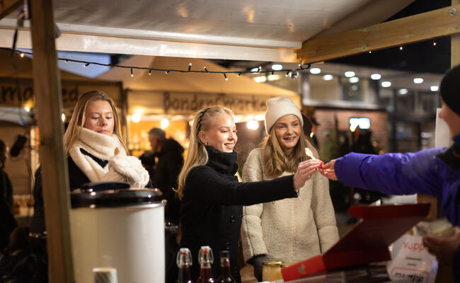 Julefestivalens stemningsfulle julemarked Foto av tre jenter som får smaksprøver fra en bod