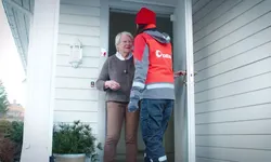 En eldre kvinne får besøk av en postansatt hjemme på døra.