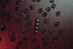 Løse tastaturtaster er lagt utover en mørk treflate. Midt i bildet danner tastene ordet «SCAM» (svindel). Motivet illustrerer digital kriminalitet og faren for svindel på nettet.