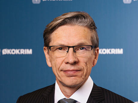 Portrettbilde av Gunnar. Han er alvorlig. Bakgrunnen er blå med Økokrims logo og løve.